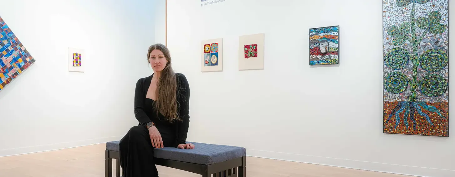 An art student sitting on a bench in a gallery. The exibit around her features her artwork.