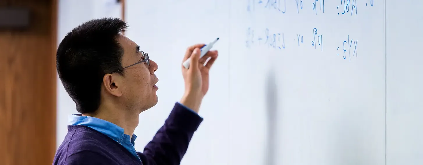 A professor writing on a whiteboard in a math course.